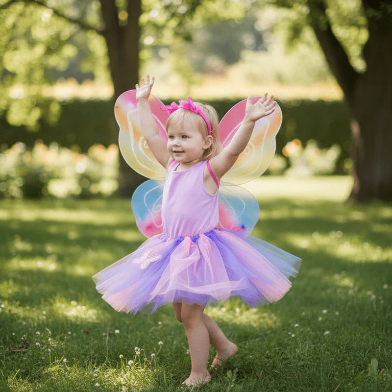 Child in a colorful fairy costume with wings standing on grass