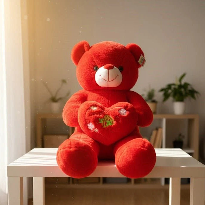 Red teddy bear with a heart on a white table in a room with plants.